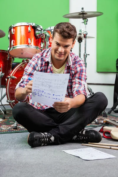 Барабанщик пишет заметки на бумаге, сидя на полу — стоковое фото