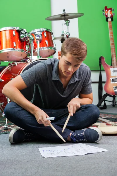 Homem praticando com bastões de tambor enquanto olha para as notas — Fotografia de Stock