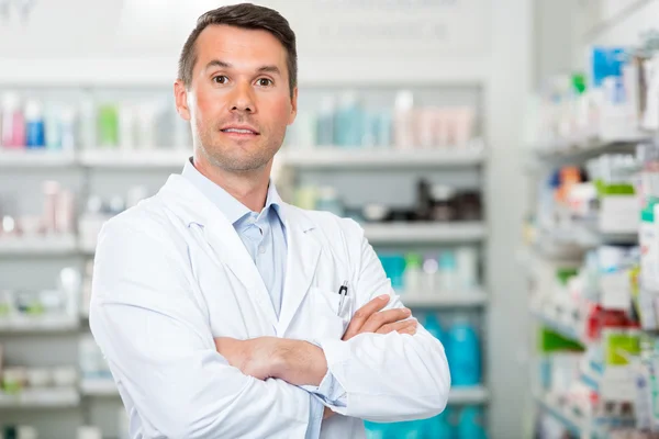 Manliga farmaceut med armar korsade står i apotek — Stockfoto