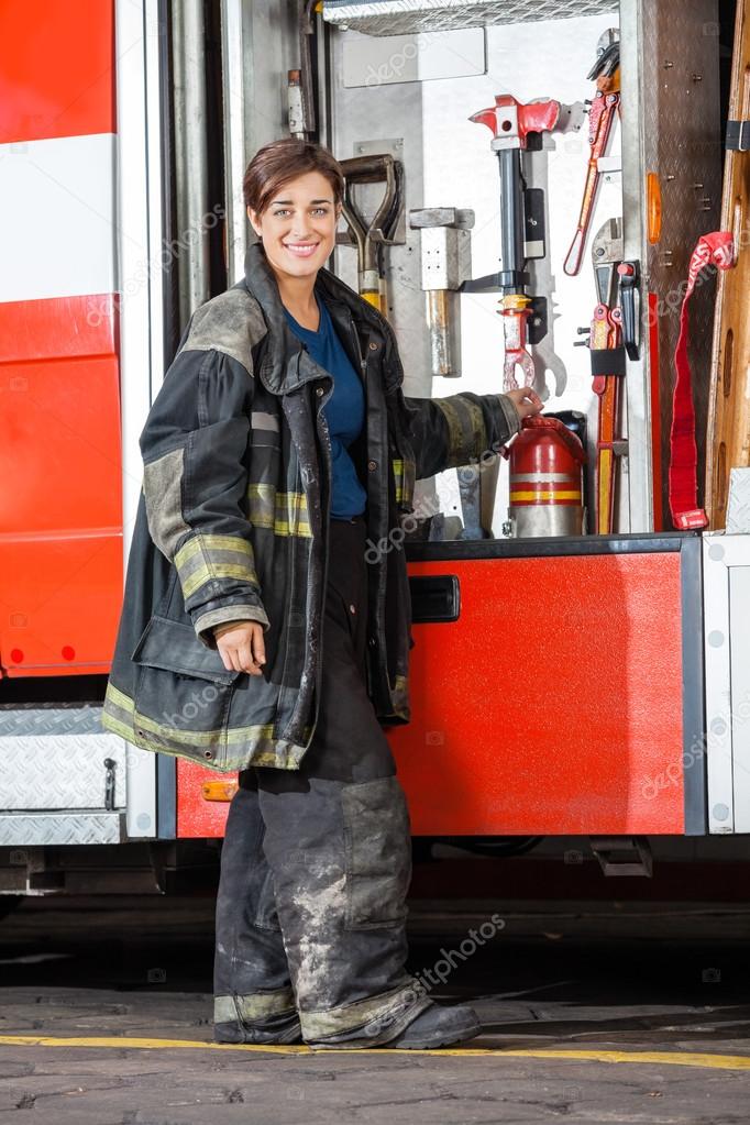 Happy Firewoman Standing By Truck At Fire Station