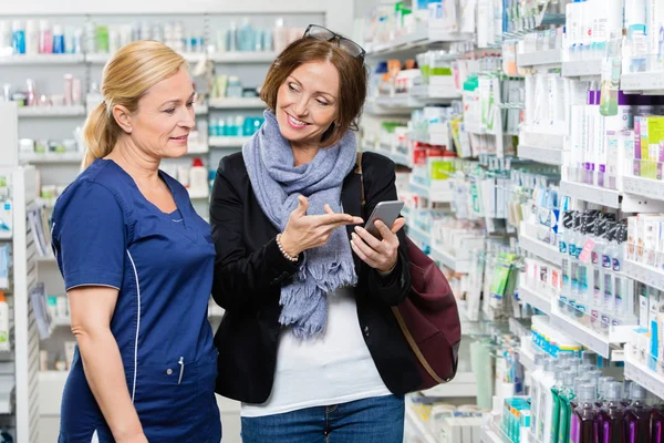 Cliente que muestra el teléfono móvil al químico en la farmacia — Foto de Stock