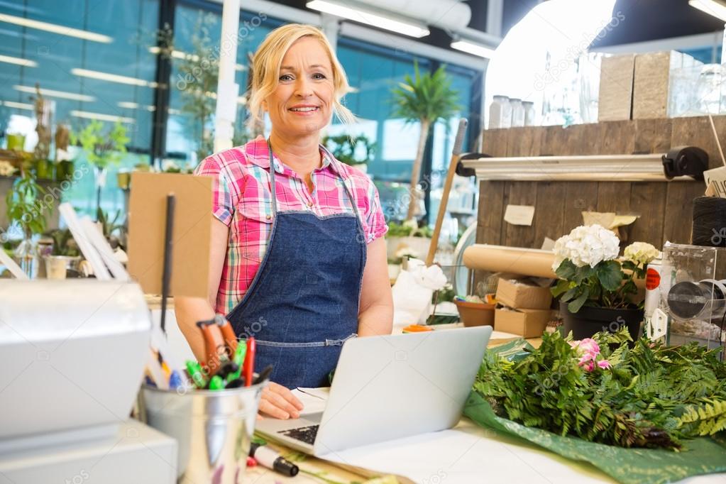 Smiling Florist Using Laptop At Counter In Flower Shop