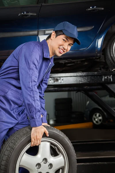 Mecánico que lleva el neumático del coche en taller de reparación de automóviles —  Fotos de Stock