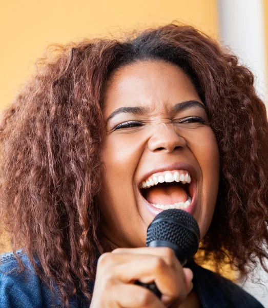 Emocionado mujer joven cantando mientras sostiene micrófono — Foto de Stock