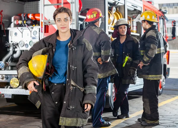 Confiado Firewoman sosteniendo el casco mientras sus colegas discuten B —  Fotos de Stock