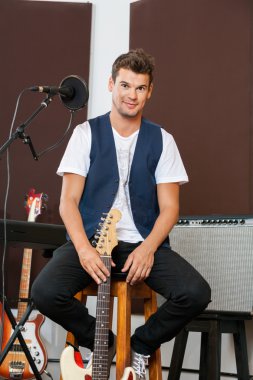 Kendine güvenen adam taburede oturan süre gitar Holding