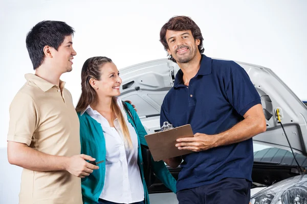 Smiling Mechanic Holding Clipboard while Standing With Couple — стоковое фото