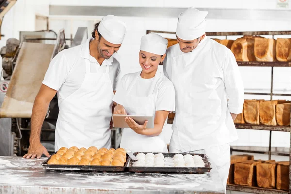 Panettieri che utilizzano tavoletta digitale durante la preparazione di pane in panetteria — Foto Stock