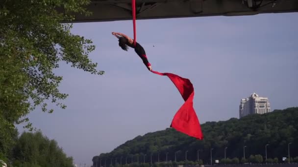 Acrobate féminin flexible faisant un tour fou et dangereux avec de la soie aérienne rouge sur le fond du ciel. Concept de désir et de passion — Video