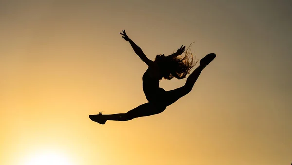 Női rugalmas táncos ugrás napnyugtakor a narancssárga égbolt hátterében. A szabadság és a boldogság fogalma — Stock Fotó