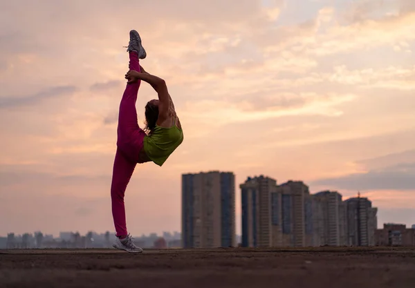 Mujer flexible haciendo split al aire libre en el dramático fondo de la puesta del sol. Concepto de yoga, estilo de vida saludable y estiramiento — Foto de Stock