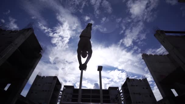 Człowiek skaczący z jednej ręki do drugiej na cyranach cyrkowych na niebie i tle budowlanym. Koncepcja stojaka na rękę, wykonania i sztuki — Wideo stockowe