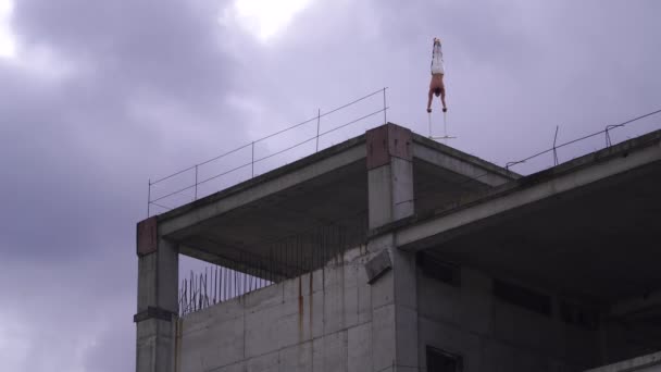 Artis sirkus yang kuat menjaga keseimbangan dengan satu tangan di tepi atap terhadap awan yang menakjubkan. Konsep risiko, keberanian dan kontrol — Stok Video