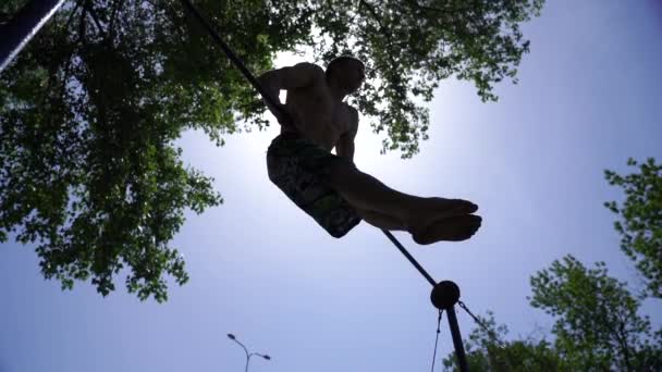 Silhouette de l'homme fort et musclé faisant Muscle-up sur la barre horizontale au ralenti sur le ciel bleu et le fond du soleil. Concept de mode de vie sain et calisthénique — Video