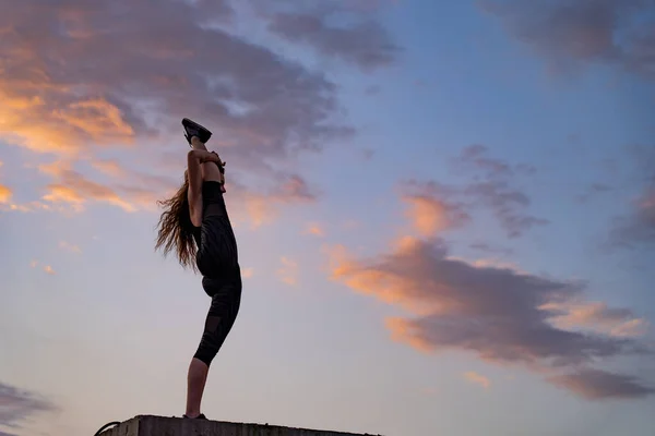 Bailarina femenina flexible en el borde de la azotea sobre el dramático fondo del cielo durante la puesta del sol. Concepto de estilo de vida saludable, talento y aspiración — Foto de Stock