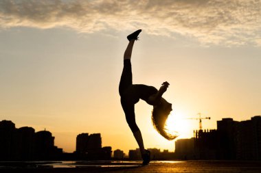 Kadın dansçı, gün batımında şehrin arka planında esnekliğini gösteriyor ve suda yansıyor. İrade ve fırsat kavramı 