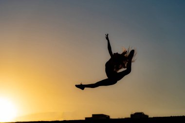 Turuncu gökyüzü arka planında günbatımında zıplayan esnek kadın dansçı. Fırsat ve motivasyon kavramı 