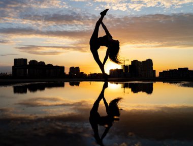Kadın dansçı, gün batımında şehrin arka planında esnekliğini gösteriyor ve suda yansıyor. Özgürlük ve mutluluk kavramı 
