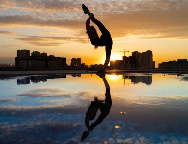 Kadın dansçı, gün batımında şehrin arka planında esnekliğini gösteriyor ve suda yansıyor. Özgürlük ve mutluluk kavramı 