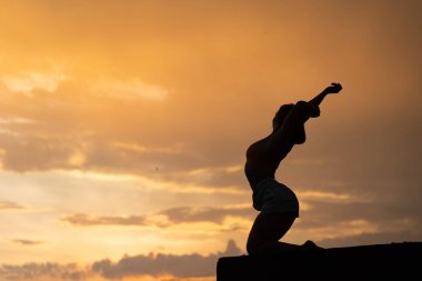 Dramatik günbatımında gökyüzü arka planı üzerinde egzersiz yapan esnek bir kız.