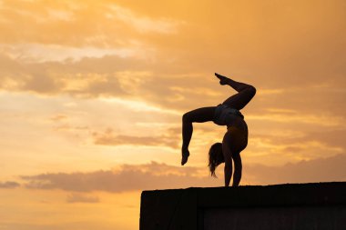 Dramatik günbatımında gökyüzü arka planı üzerinde egzersiz yapan esnek bir kız.