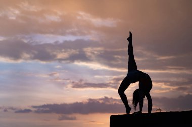 Dramatik günbatımında gökyüzü arka planı üzerinde egzersiz yapan esnek bir kız.