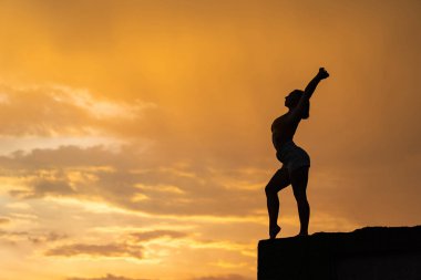 Dramatik günbatımında gökyüzü arka planı üzerinde egzersiz yapan esnek bir kız.