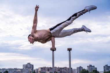 Sirk sanatçısı bir elinde bulutlu arka planda dengesini koruyor. Amuda kalkmak, performans ve sanat anlayışı