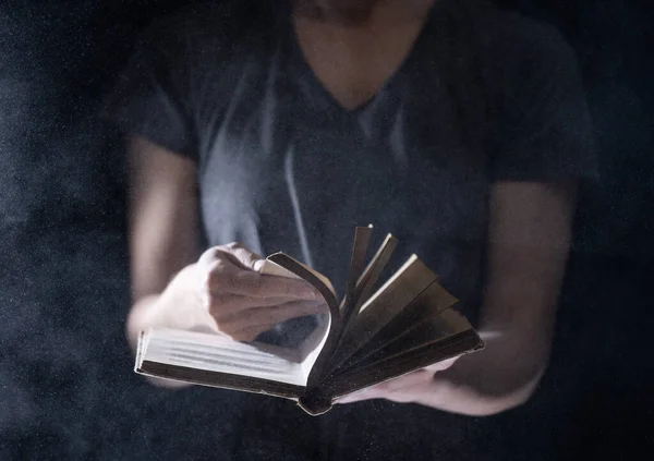 Hands hold Vintage open Book Glows on black background. Concept of mystery, riddle and secret