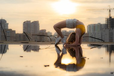 Esnek kadın jimnastikçi dramatik günbatımında suda yansıma numarası yapıyor.