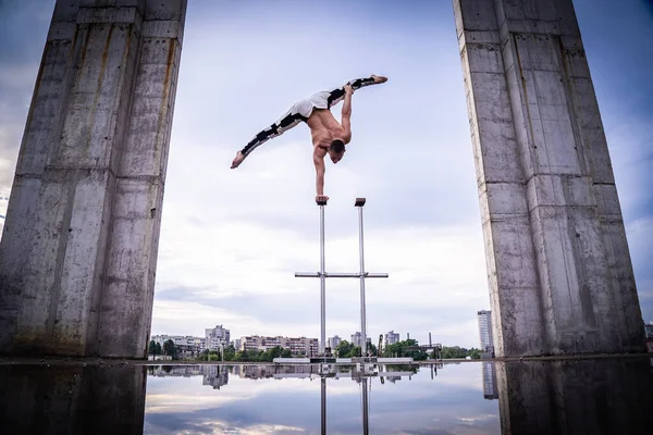 Circus artist keeps balance on one hand on the sky and industrial construction background. Concept of handstand, performing and art
