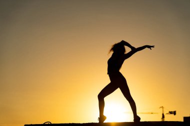  Çatı katının kenarında, turuncu gökyüzü arka planında dans eden kadın dansçı. Neşe ve arzu kavramı 