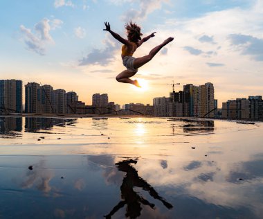 Gün batımında şehrin arka planında suda yansıyan esnek kadın dansçı. Özgürlük ve mutluluk kavramı 