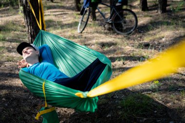 Şapkalı genç adam dışarıda, hamakta, ormanda dinleniyor..