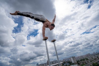 Esnek erkek sirk sanatçısı inanılmaz bulutlara karşı çatıda tek elle dengesini koruyor. İrade, potansiyel ve arzu kavramı