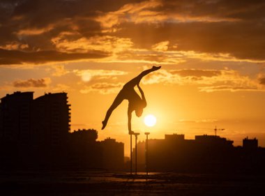 Esnek kadın sirk sanatçısı dramatik günbatımına ve şehir manzarasına karşı çatıda denge kuruyor ve kıvrılıyor. Motivasyon, tutku ve başarı kavramı 
