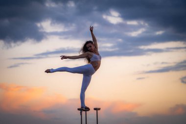 Esnek ve zinde bir kız silueti. Yoga ve sağlıklı yaşam tarzı kavramının dramatik günbatımına karşı bölünmüş ve dengesini koruyor. 