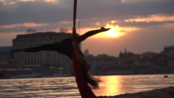 女性ダンサーのシルエットは彼女の柔軟性を示し、劇的な空の下で街の背景に赤い空のシルクで分割します。情熱、欲望、魅力の概念 — ストック動画