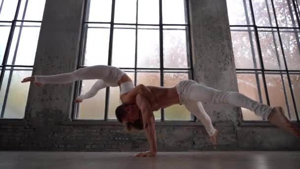 Acrobatic duet robi ładną pozę na tle ogromnych okien z jesiennymi drzewami pomarańczowymi na zewnątrz. Pojęcie relacji, szczęścia i zaufania — Wideo stockowe