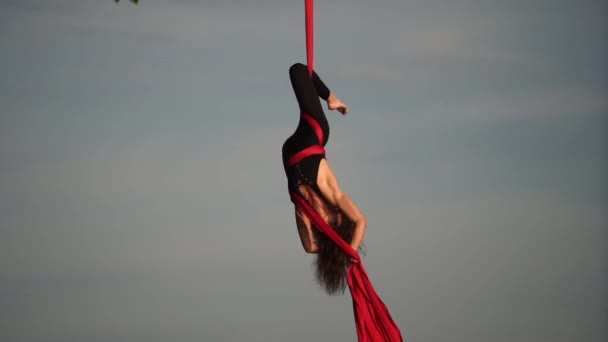 Acrobata femminile mostrando la sua flessibilità e si divide con seta aerea rossa sullo sfondo del cielo. Concetto di grazia, movimento e bellezza — Video Stock