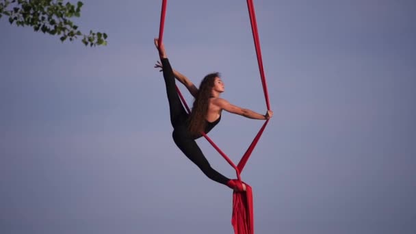 Kvinnlig akrobat visar sin flexibilitet och delar sig med rött antenn silke på himlen bakgrund. Begreppet nåd, rörelse och skönhet — Stockvideo