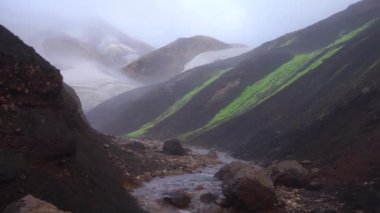 Buzul parçalı görkemli bir manzara, renkli bir jeolojik yapı ve yavaş çekimde geçen küçük bir nehir. Laugavegur yürüyüş yolu, İzlanda
