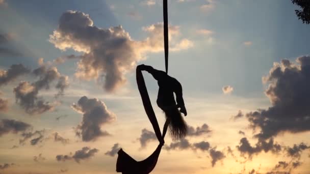 Artista de circo feminina mostrando sua flexibilidade e se divide com seda aérea vermelha no fundo do céu. Conceito de estilo de vida saudável — Vídeo de Stock
