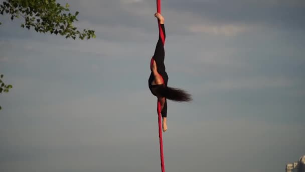 Женщина-акробат демонстрирует свою гибкость и расщепляется с красным воздушным шелком на фоне неба. Понятие грации, движения и красоты — стоковое видео