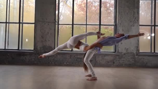 Acrobatic duet robi ładną pozę na tle ogromnych okien z jesiennymi drzewami pomarańczowymi na zewnątrz. Pojęcie relacji, szczęścia i zaufania — Wideo stockowe