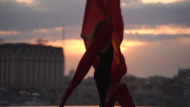 Silueta ženské tanečnice ukazující svou pružnost a štěpí se červeným leteckým hedvábím na pozadí města během dramatické oblohy. Pojetí vášně, touhy a přitažlivosti — Stock video