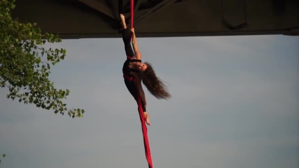 Zirkusartistin, die ihre Flexibilität zeigt und sich mit roter Antennenseide auf dem Himmelshintergrund teilt, ist Zeitlupe. Konzept eines gesunden Lebensstils — Stockvideo