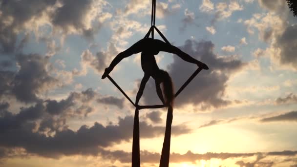 Silhouette of Female circus artist showing her flexibility and splits with red aerial silk on the dramatic sky background. Concept of movement and motion — Stock Video