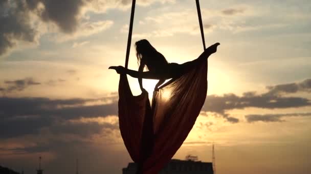 Sylwetka artystki cyrku kobiecego ukazująca swoją elastyczność i rozszczepia się czerwonym powietrznym jedwabiem na dramatycznym tle nieba. Koncepcja ruchu i ruchu — Wideo stockowe