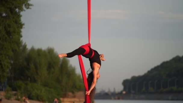 Цирковая артистка демонстрирует свою гибкость и расщепляется с красным воздушным шелком на фоне неба - замедленная съемка. Концепция здорового образа жизни — стоковое видео